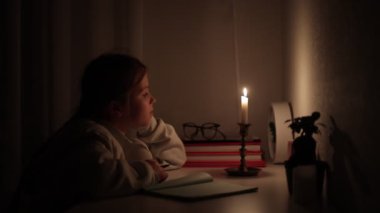 Elektriksiz bir karanlıkta kız öğrenci mesafesini evde öğreniyor. Genç çocuk bilinç kaybı sırasında okul ödevini yapmak için mum ışığını kullanıyor. Enerji krizi konsepti. Ukrayna 'da elektrik kesintisi.