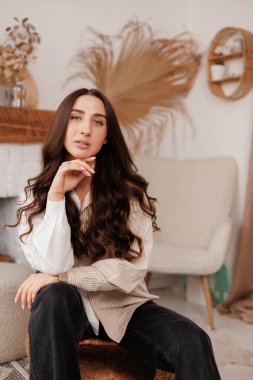 Çekici, kendine güvenen, şık, uzun saçlı esmer kadın kırsal tarzda yaratıcı tasarımı olan oturma odasına bakıyor. Güzellik, moda, kendini ifade etme, bireysellik kavramı