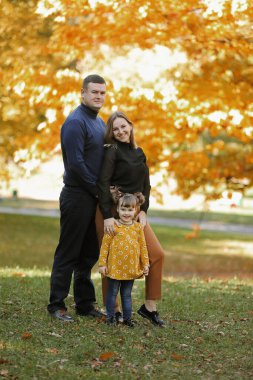 Aile günü. Mutlu genç anne ve baba küçük kızlarının ellerini tutarak yürür, sonbahar parkında eğlenir, hafta sonları birlikte vakit geçirirler. Ebeveyn sevgisi, ruh sağlığı ve mutlu bir yaşam tarzı..