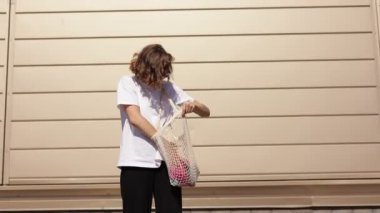 Endişeli genç bir kadın açık havada pamuk alışveriş torbasında smth arıyor. Moda çevre dostu aksesuar. Milenyum dişisi yeniden kullanılabilir ip torbası taşıyor. Alternatif plastik yaşam tarzı kavramı yok.