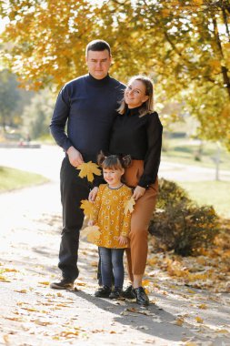 Aile günü. Mutlu genç anne ve baba küçük kızlarının ellerini tutarak yürür, sonbahar parkında eğlenir, hafta sonları birlikte vakit geçirirler. Ebeveyn sevgisi, ruh sağlığı ve mutlu bir yaşam tarzı..