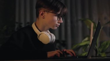 Gözlüklü, kulaklıklı, klavyeli genç bilgisayar oyuncusu, bilgisayar oyunları, esportlar, karanlık odada dizüstü bilgisayara aşırı yakın oyunlar oynuyor. Z jenerasyonunda vizyon zayıf.