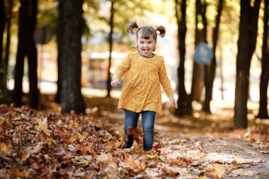 Çocuk günü. Komik saçlı, sarı çiçekli iki atkuyruklu neşeli kız çocuğu. Eğleniyor, gülümsüyor, güneşli sonbahar parkında yürümekten hoşlanıyor. Çocukluk hayali konsepti.