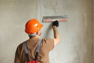 Tulum giymiş tamirci ve koruyucu miğfer takmış, macun bıçağıyla beton duvarları sıva ile sıvanmış. Dairenin yenilenmesi ve yeni bina konsepti