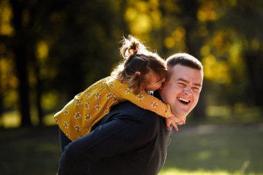Neşeli baba gülümseyen kızına sarılıyor. Bekar baba ve çocuk sonbahar parkında eğleniyor, gülüyor ve doğanın tadını çıkarıyor. Ebeveyn bakımı ve tasasız çocukluk kavramı. Babalar günün kutlu olsun..