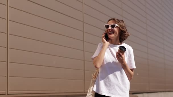 Ξέγνοιαστη Νεαρή Γυναίκα Κομψά Γυαλιά Ηλίου Μιλάει Στο Smartphone Γελάει — Αρχείο Βίντεο