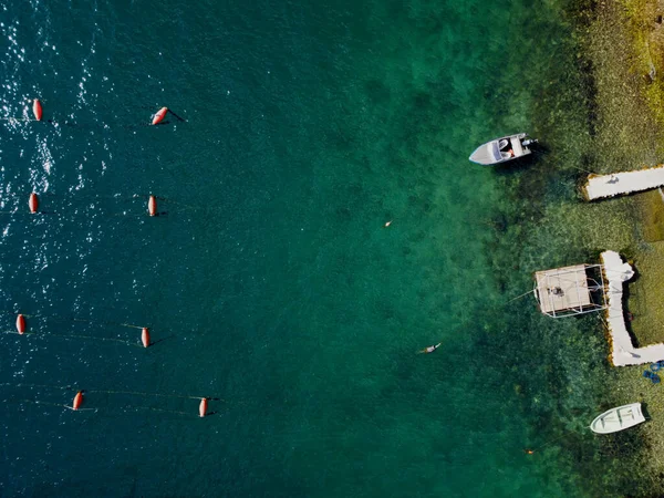 Aerial top down view of three fishing boats parked by the pier on the tropilal seashore. Drone flying over shoreline and sea surface with transparent turquoise water with sun reflections