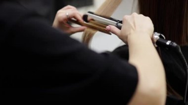 Tanımlanamayan profesyonel kuaför. Saç düzleştirici ve tarak ile kadın saçı ütülüyor. Güzellik salonunda şık bir saç stili yapıyor. Keratin, laminasyon, saç bakımı, kuaför salonu ve kuaförlük.