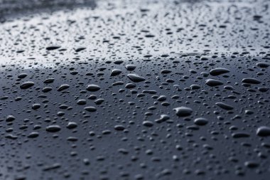 Soyut yağmur veya su, parlak yansımalı mavi bir arabanın kaput yüzeyine farklı boyutlarda düşer. Koyu demir yüzey ve doku üzerindeki su damlacıkları. Tasarım için arkaplan ve su dokusu