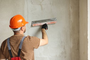 Tulum giymiş tamirci ve koruyucu miğfer takmış, macun bıçağıyla beton duvarları sıva ile sıvanmış. Dairenin yenilenmesi ve yeni bina konsepti