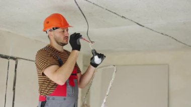 Üniformalı elektrik, koruyucu eldivenler ve tornavida ile elektrik voltajının kontrol edilip ölçülmesi. Yeni binadaki kabloları voltaj dedektörüyle inceliyorum..