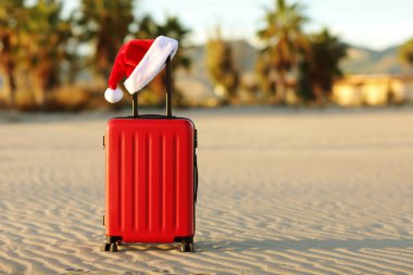 İçinde Noel Baba 'nın kırmızı şapkası olan kırmızı bavul tropikal kumsal, palmiyeler, dağlar ve deniz altyapısı olan. Noel tatili ve yeni yıl için seyahat konsepti. Mesaj için yer. İndirimli geziler.