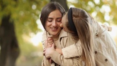 Aile günü. Genç anne ve küçük kızı sonbahar parkında eğleniyor ve dinleniyor. Sevimli kız çocuğu sıkıca sarılıyor ve annesini öpüyor. Çocuğa annelik ve sevgi. Anneler Günü.