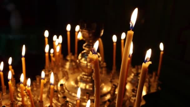 关闭在东正教教堂燃着的蜡烛 纪念蜡蜡烛闪烁着火焰在巨大的金烛台上 在庙宇的黑暗中闪烁着 宗教和信仰的概念 — 图库视频影像