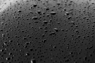 Yağmur ya da su, siyah, parlak bir arabanın kaput yüzeyine farklı boyutlarda düşer. Koyu demir yüzey ve doku üzerindeki su damlacıkları. Tasarım için soyut arkaplan ve su dokusu