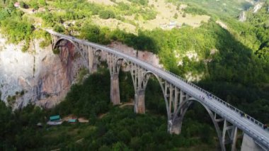 Karadağ 'daki Tara nehri kanyonu üzerinde hareket eden arabalarla Kemerli Curdjevica Köprüsü' nün hava aracı görüntüsü, yazın yeşil manzara. Durmitor Milli Parkı 'ndaki Zabljak kasabası yakınlarındaki popüler turizm beldesi
