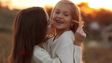 Aile günü, anneler günü. Mutlu gülümseyen genç anne ve sevimli kız çocuğu gün batımında sarılıyor, öpüşüyor ve birlikte vakit geçiriyorlar. Idyllic ailesi sonbahar tatilinde dışarıda eğleniyor.