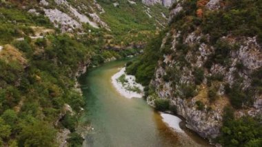Karadağ 'ın turkuaz nehri ile güzel kayalık bir kanyonun ortasındaki asma eski metal köprünün hava aracı görüntüsü. Moraca nehri kanyonu yeşil canlı bitki örtüsüyle