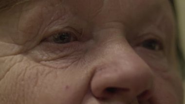 Kafkasyalı yaşlı bir kadının yüzünü ve gözlerini kapat. Yaşlı kadınların yüzünde büyük kırışıklıklar var. Yorgun ve üzgün bakışları olan yaşlı bir vatandaş uzaktan bakıyor ve göz kırpıyor.
