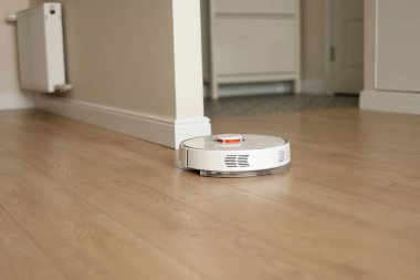 Modern kablosuz otonom robot elektrikli süpürge oturma odasını temizliyor. Akıllı oto itişli beyaz temizlik robotu ahşap zemini yıkıyor. Uzaktan kumandalı ev aletleri