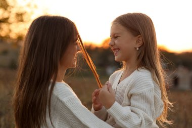 Aile günü, anneler günü. Mutlu gülümseyen genç anne ve sevimli kız çocuğu gün batımında sarılıyor, öpüşüyor ve birlikte vakit geçiriyorlar. Idyllic ailesi sonbahar tatilinde dışarıda eğleniyor.