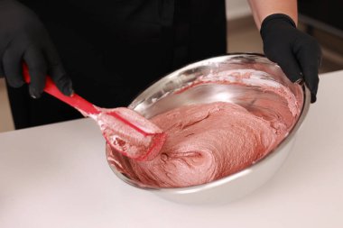 The pastry chef mixes silicone spatula the brown dough for the French desert macaron or macaroon in a stainless steel bowl, the process of preparing the cakes. Concept of confectionery or pastry shop.