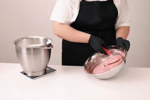 The pastry chef mixes silicone spatula the brown dough for the French desert macaron or macaroon in a stainless steel bowl, the process of preparing the cakes. Concept of confectionery or pastry shop.