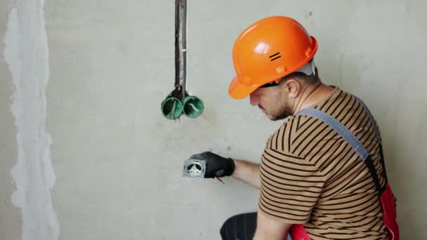 制服の電気技師男性 保護手袋 ヘルメットは ソケット段階の電圧の存在をチェックする電気テスターのスクリュードライバーを使用します 電圧検出器によって出口のワイヤーを検査する屋内 — ストック動画