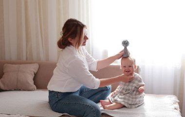 Genç, gülümseyen anne ve bebek birlikte vakit geçirip evde oyun oynuyorlar. İlk bebek adımları. Küçük kızımla yakın ilişki. Anneler Günü. Uluslararası Çocuk Günü..