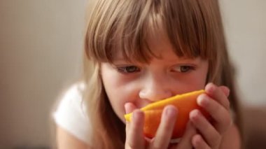 Sevimli kız çocuğunun portresi portakal yiyor. Küçük çocuk evde aç gözlülükle portakal yiyor. meyveli sağlıklı çocuk konsepti. rüya sulu meyve portakalları sağlıklı beslenmek içindir.