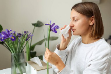 Alerjisi olan genç bir kadın süsen çiçeğini tutuyor. Burnu kağıt mendille kaplı. Burnu akıyor. Grip olmuş, kaşınan, öksüren, mevsimsel alerjisi olan bir kız..
