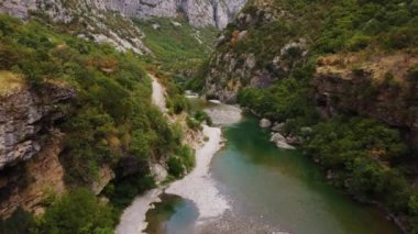 Karadağ 'ın turkuaz nehri ile güzel kayalık bir kanyonun ortasındaki asma eski metal köprünün hava aracı görüntüsü. Moraca nehri kanyonu yeşil canlı bitki örtüsüyle