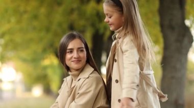 Aile günü. Genç anne ve küçük kızı sonbahar parkında eğleniyor ve dinleniyor. Sevimli kız çocuğu sıkıca sarılıyor ve annesini öpüyor. Çocuğa annelik ve sevgi. Anneler Günü.