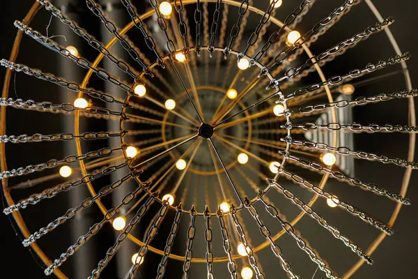 Çatı katının tavanında metal zincirler ve sıcak ampullerden yapılmış yuvarlak siyah avize. Alt görünüm klasik dekor. İç yapı kavramı çağdaş