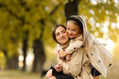Aile günü. Genç anne ve küçük kızı sonbahar parkında eğleniyor ve dinleniyor. Sevimli kız çocuğu sıkıca sarılıyor ve annesini öpüyor. Çocuğa annelik ve sevgi. Anneler Günü.