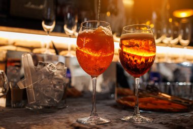 Tezgahta iki bardak Aperol Spretz kokteyli. Tipik İtalyan içeceği, Prosecco köpüklü beyaz şarap, buz ve taze portakal dilimleriyle yapılan aperatif. Turuncu sıvı karıştırılıyor