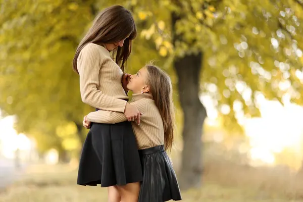 Aile günü. Genç anne ve küçük kızı sonbahar parkında eğleniyor ve dinleniyor. Sevimli kız çocuğu sıkıca sarılıyor ve annesini öpüyor. Çocuğa annelik ve sevgi. Anneler Günü.
