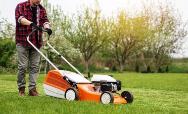 Sıradan giysiler içinde bir adam evinin arka bahçesinde çim biçme makinesiyle çim biçiyor. Baharın bulutlu olduğu bir günde koca bahçeyle ilgilenir. Modern benzin bahçesi ekipmanları. Peyzaj işi.