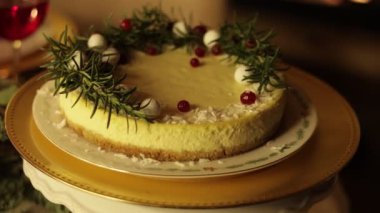 Noel şenlikli cheesecake süslenmiş biberiye dalları, yaban mersini ve beyaz toplar altın tabakta. Ev yapımı kırsal tatlı. Kamera hareket ediyor. Yeni yıl partisini evde kutluyoruz..