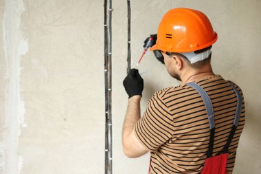 Erkek elektrikçi, prizdeki elektrik voltajını kontrol ediyor. Elektrikli tornavida kullanıyor. İçerideki voltaj dedektörüyle prizdeki üç renkli kabloyu inceliyorum..