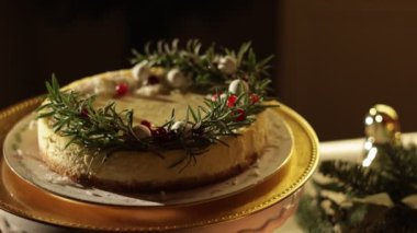 Noel şenlikli cheesecake süslenmiş biberiye dalları, yaban mersini ve beyaz toplar altın tabakta. Ev yapımı kırsal tatlı. Kamera hareket ediyor. Yeni yıl partisini evde kutluyoruz..