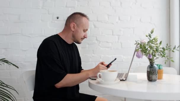 즐거운 남자는 커피숍이나 오피스에서 테이블에 전화를 노트북에서 작업에서 즐거운 온라인 — 비디오