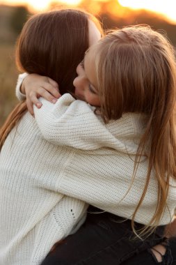Aile günü, anneler günü. Mutlu gülümseyen genç anne ve sevimli kız çocuğu gün batımında sarılıyor, öpüşüyor ve birlikte vakit geçiriyorlar. Idyllic ailesi sonbahar tatilinde dışarıda eğleniyor.