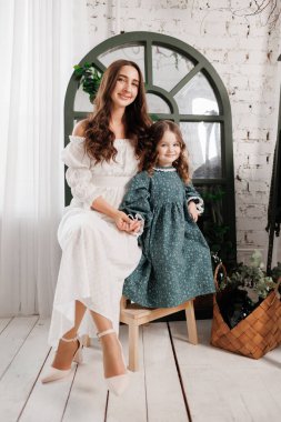 Anneler Günü. Zarif genç anne ve küçük tatlı kız evdeki oturma odasında tahta sandalyeye oturup gülümser ve kameraya bakarlar. Anneyle çocuk arasındaki güven, destek ve sevgi. Çocuk günü.