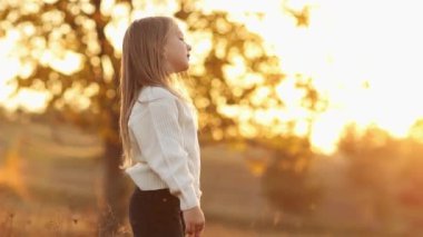 Çocuklar Günü 'nde. Neşeli küçük beyaz kız 5-6 yaş arası temiz hava soluyor, stresi azaltıyor, ellerini kaldırıyor, sonbahar günbatımında doğada tatilin tadını çıkarıyor. Boş zaman aktivitesi