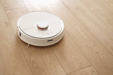 Beyaz kablosuz otonom robot elektrikli süpürgenin ahşap zemindeki en üst görüntüsü. Akıllı temizlik teknolojisi. Otomatik itişli temizlik robotu. Yer temizleme sistemi. Ev kumandası aygıtları