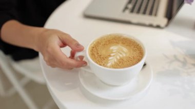Kahve molası. Genç bir kadın elinde sütü kapalı bir fincan kahve ile evde dizüstü bilgisayarla boş vakit geçirmekten hoşlanıyor. Kendine güveni olan bayan yeni başlayan yaratıcı serbest yazar uzak bir iş yerinde cappuccino tatma gevşetir.