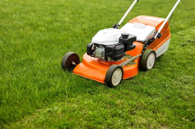 Modern turuncu-gri çim biçme makinesinin parlak yeşil çimleri biçme manzarası. Bahçıvanlık aletleri. Çimenlikteki çim biçme makinesi. Profesyonel bahçe bakımı servisi. Metin için yer.
