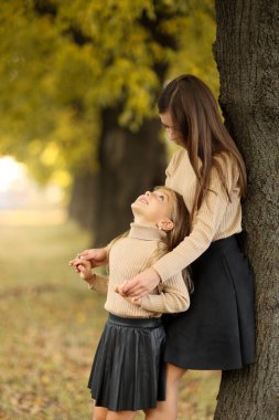 Aile günü. Genç anne ve küçük kızı sonbahar parkında eğleniyor ve dinleniyor. Sevimli kız çocuğu sıkıca sarılıyor ve annesini öpüyor. Çocuğa annelik ve sevgi. Anneler Günü.
