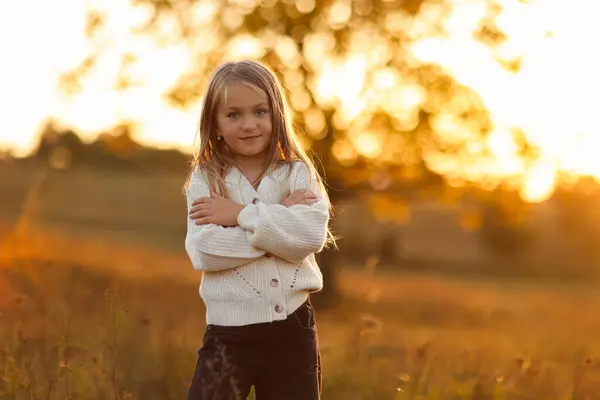 stock image Children's day. Portrait of adorable little child caucasian girl 5-6 years smiles and looks at camera with crossed hands her hand outdoors in fall sunset lights. Leisure activity on autumn holiday